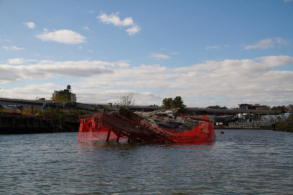 Closer look of the sunken dock on the Gowanus canal with orange fencing wrapped around it.